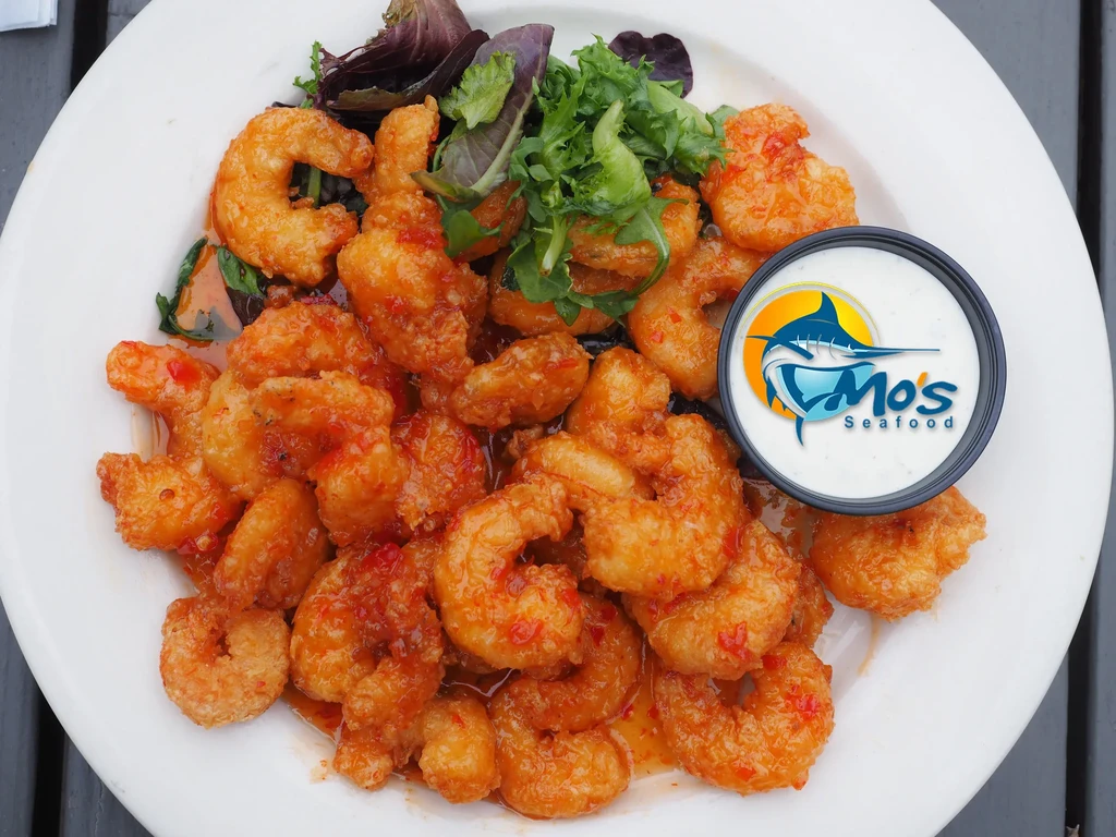 Plate of crispy breaded shrimp with red sauce, greens, and Mo's Seafood dip.