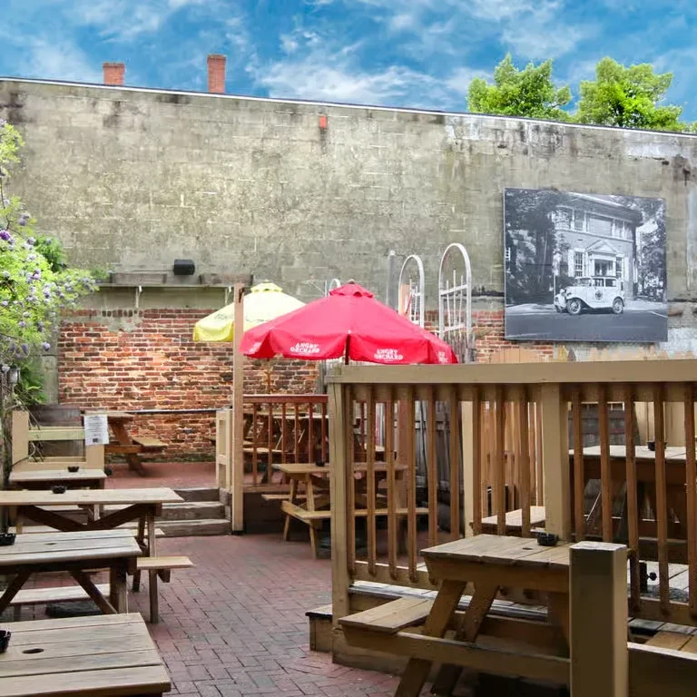 Empty outdoor patio with wooden picnic tables, colorful umbrellas, and mural.