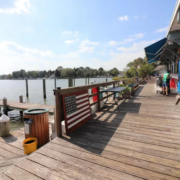 A sunny wooden waterfront deck with an American flag and distant boats.