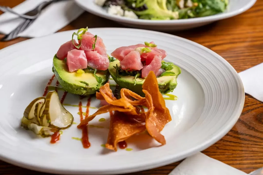 Avocado halves topped with diced fish, green onions, crisps, and sauces.