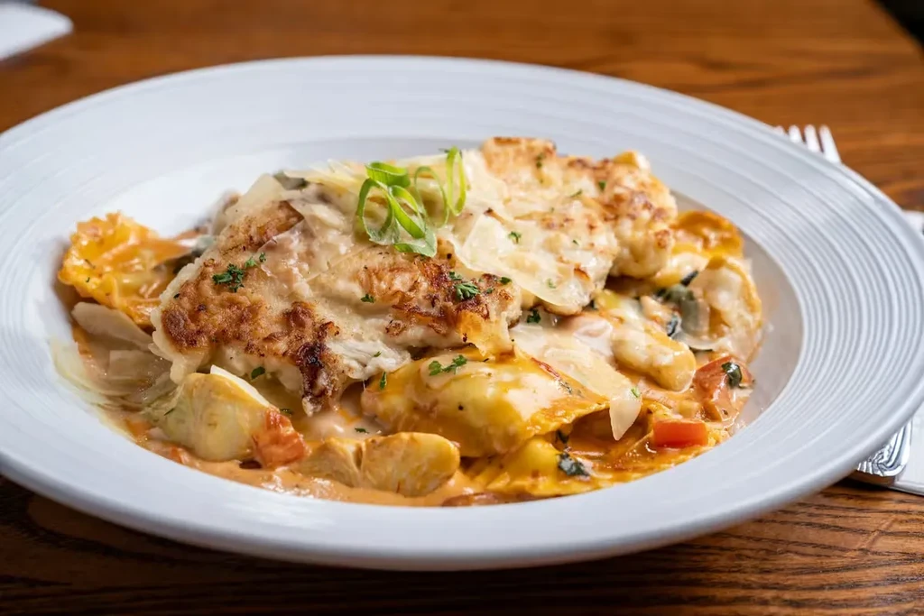 Plated ravioli with creamy sauce, crispy protein, cheese, and fresh herbs.