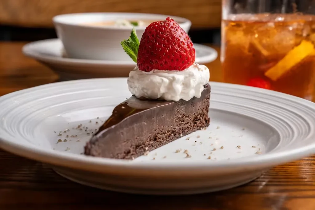 Chocolate cake slice with whipped cream, strawberry, and mint.