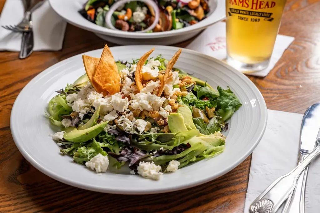 Vibrant salad with avocado, feta, and tortilla chips on a wooden table.