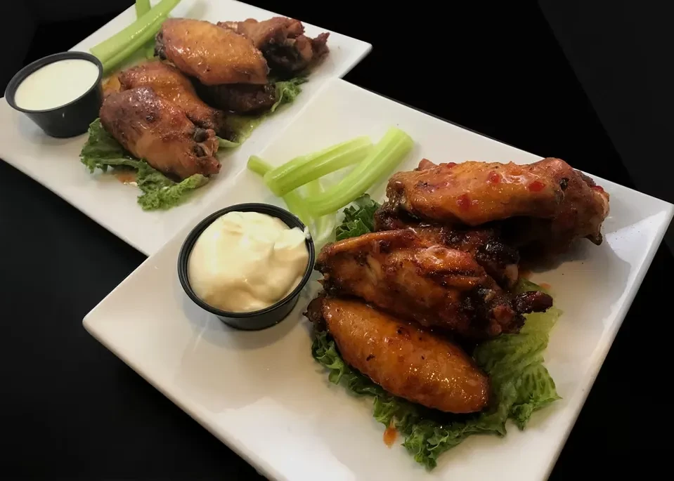Two plates of sau sauced chicken wings with lettuce, celery, and dip.
