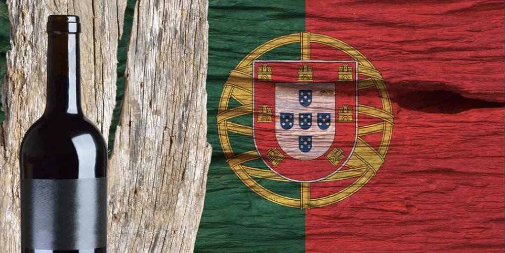 Dark wine bottle on wood, beside textured Portuguese flag.
