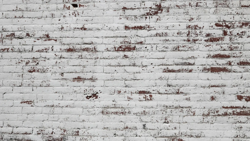 A brick wall with peeling white paint revealing red bricks.