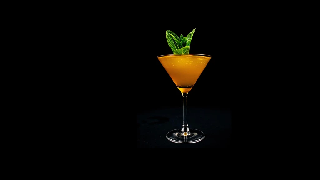 Golden cocktail in martini glass with mint on black background.