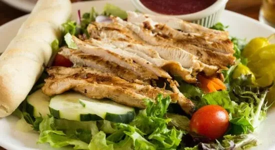 Grilled chicken salad with lettuce, cucumber, tomato, peppers, and breadstick.