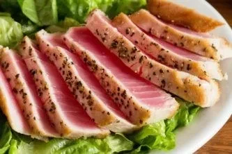 Close-up of pepper-crusted seared tuna with pink center on greens.