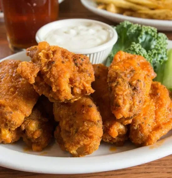 Close-up of golden-orange buffalo wings, dipping sauce, and celery on a plate.