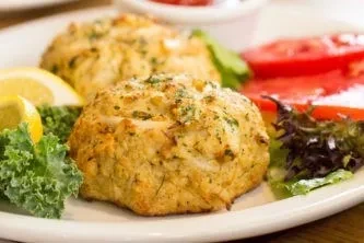 Two golden-brown crab cakes garnished with lemon, lettuce, and tomato.