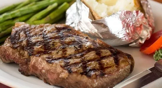 Grilled steak with grill marks, asparagus, and a foil-wrapped potato.