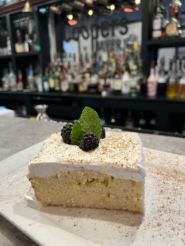 Tres leches cake slice with blackberries, mint, and cinnamon in tavern.