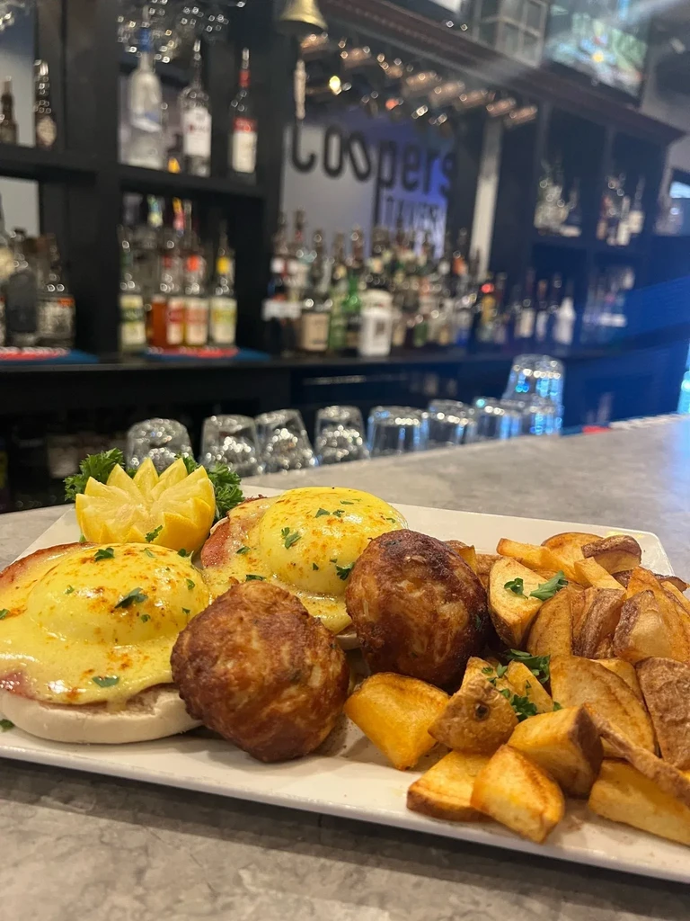 Eggs Benedict with sides and drinks at a bar.