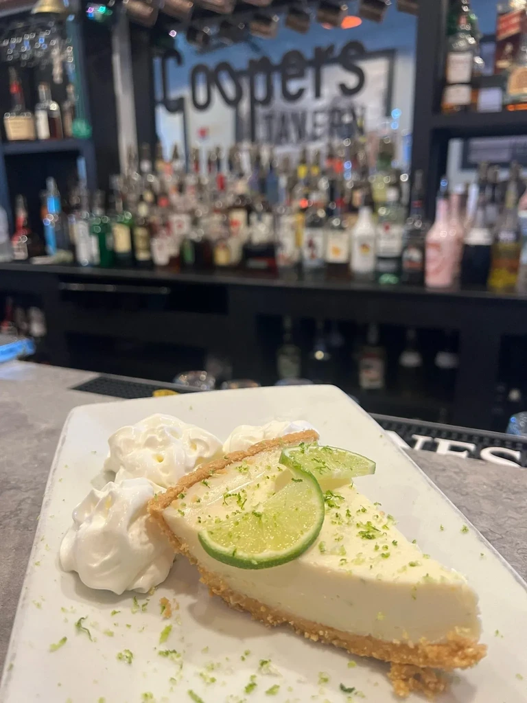 Slice of Key lime pie with whipped cream and lime garnishes.
