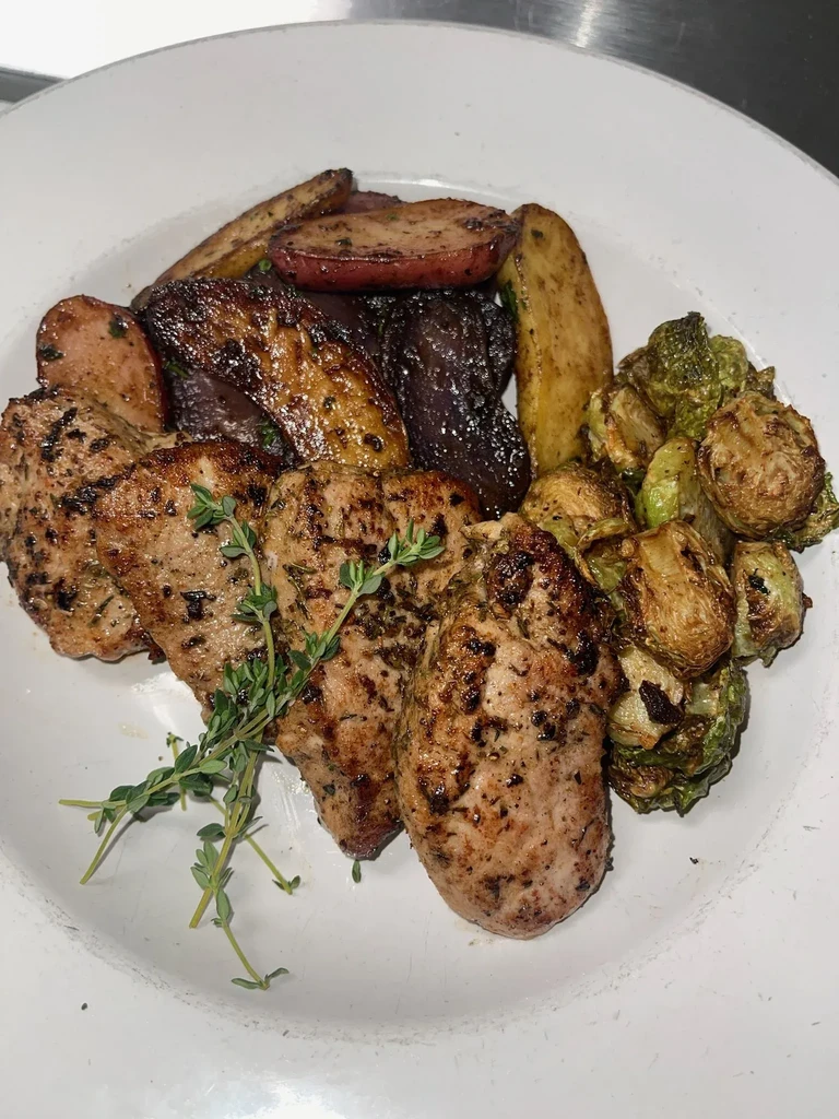 Plated grilled meat, roasted potatoes, Brussels sprouts, and root vegetables.