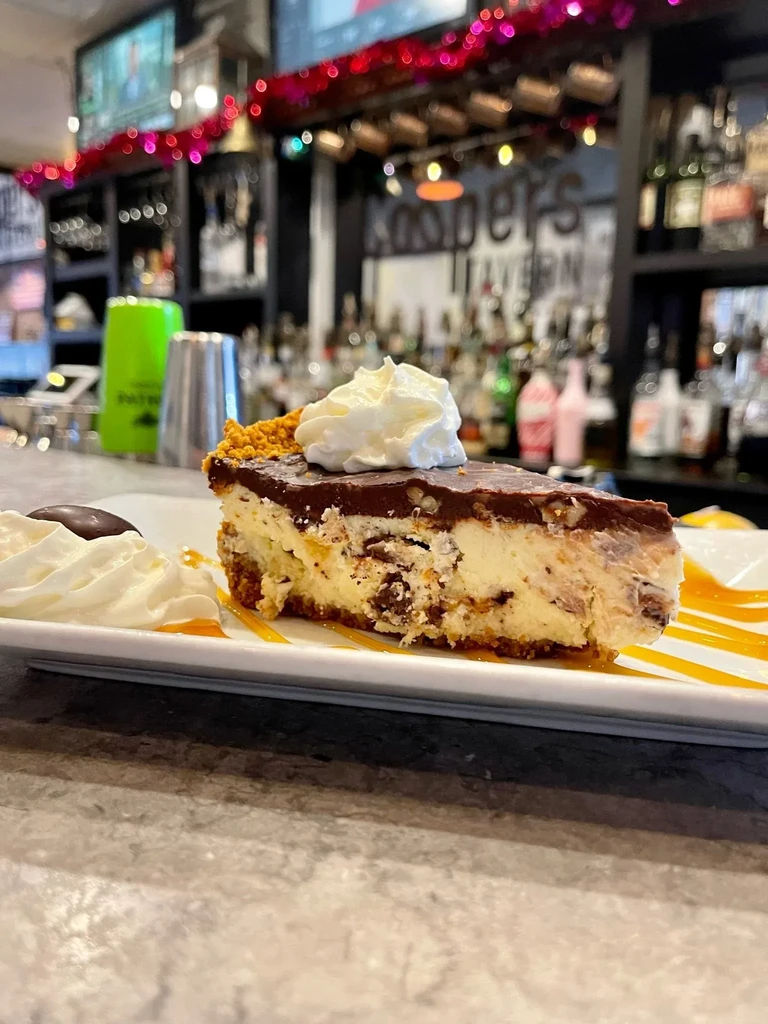 Slice of chocolate cheesecake with whipped cream and caramel at a bar.