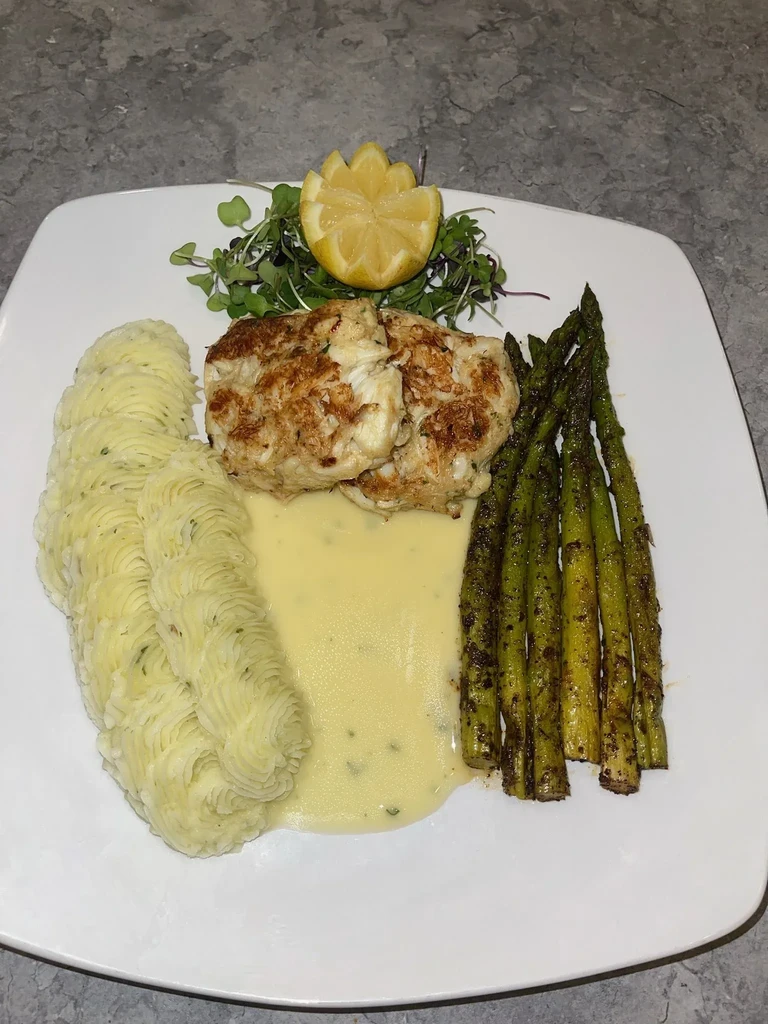 Well-plated crab cakes with mashed potatoes, asparagus, sauce, and lemon.