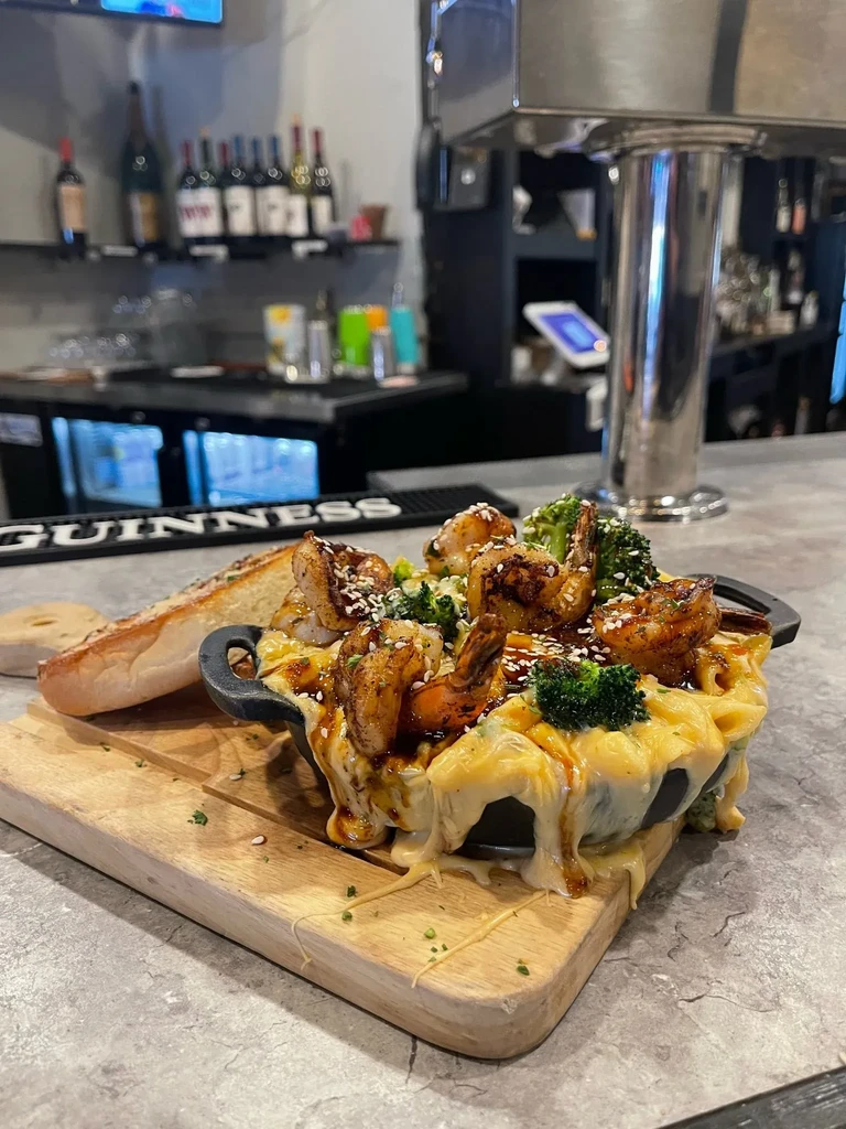 Macaroni and cheese with shrimp, broccoli, and bread on a cutting board.
