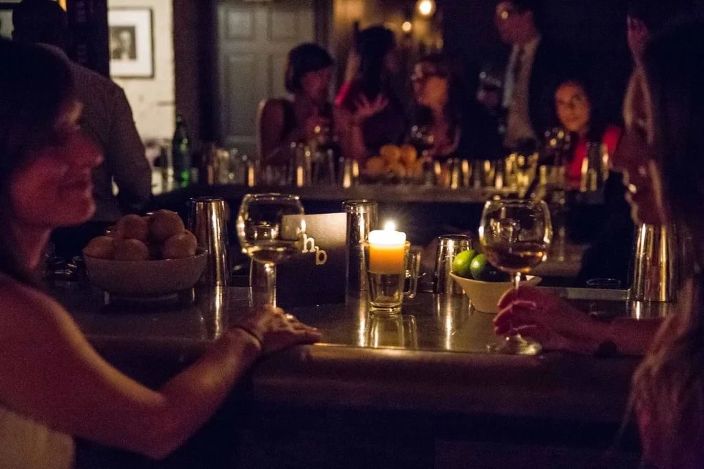 Blurred people talk at a cozy bar with wine, candle, and food.