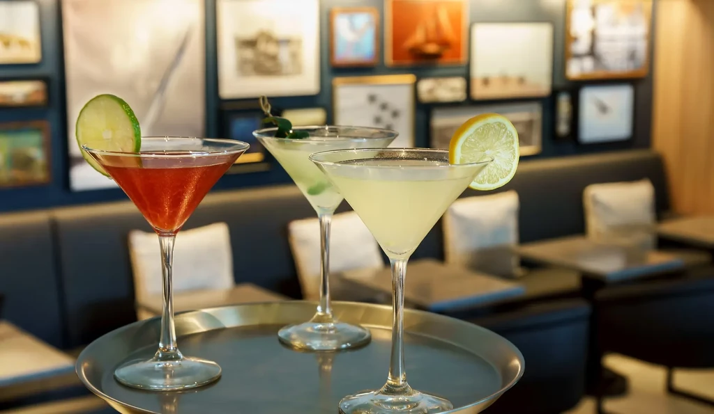 Three colorful cocktails in martini glasses on a tray in a restaurant.