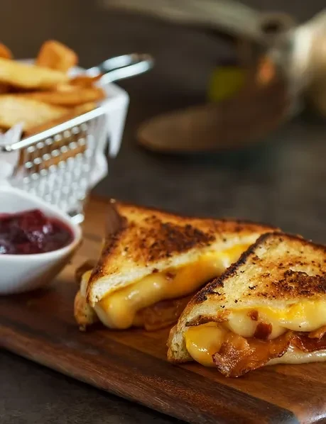 Grilled cheese with bacon, melted cheese, fries, and red sauce.