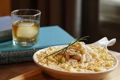 Close-up: Baked crab gratin, amber drink, and book on wood.