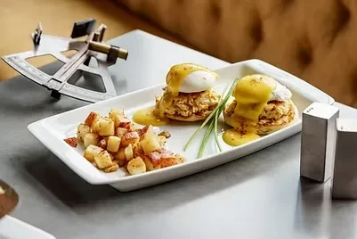 Two servings of Eggs Benedict with potatoes on a white platter.