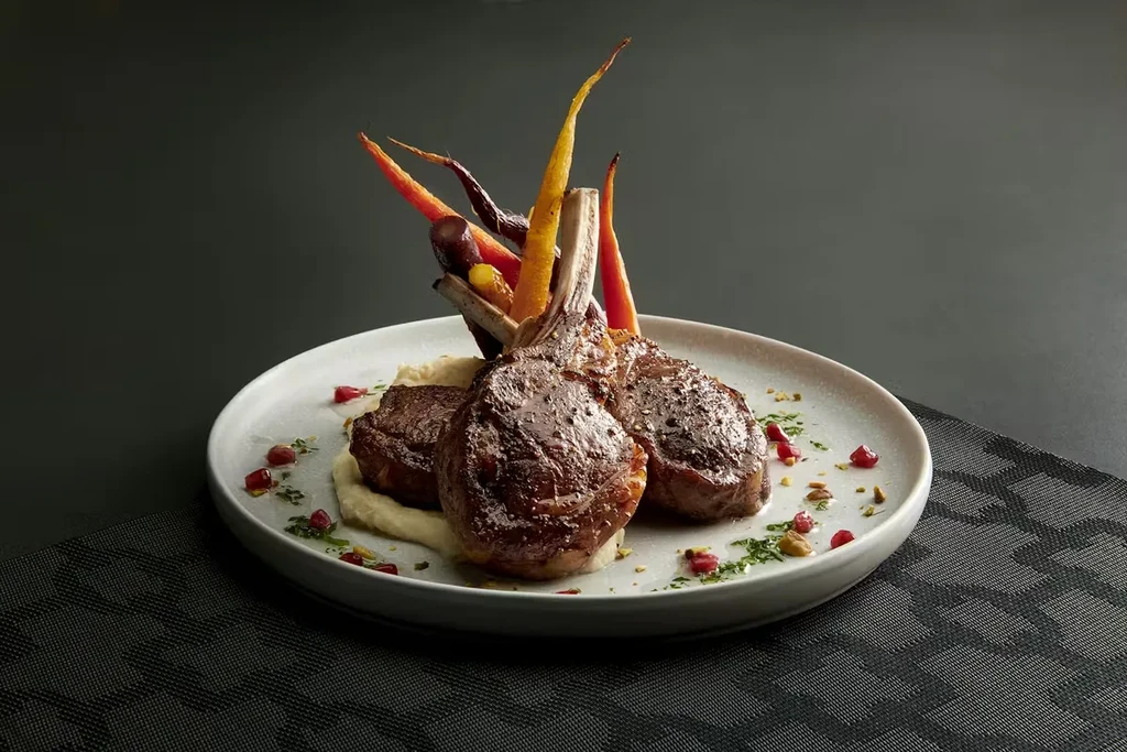 Seared lamb chops, purée, colorful roasted carrots, and pomegranate garnish.
