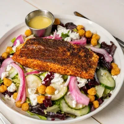 Seared salmon salad with mixed greens, pickled onions, feta, and dressing.