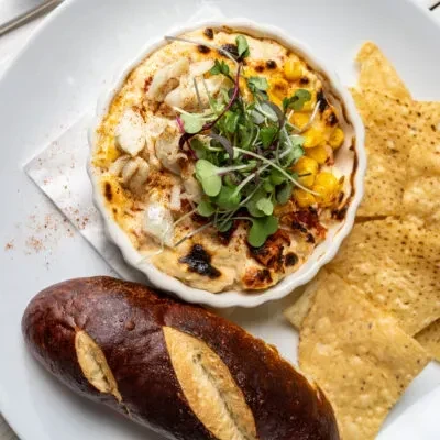 Close-up of baked crab and corn dip with pretzel bread and chips.