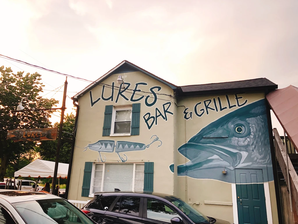 LURES BAR & GRILLE exterior, large fish murals, outdoor tent, parked cars.