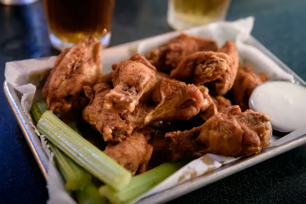 Golden-brown fried chicken wings, celery, and creamy dipping sauce in a basket.
