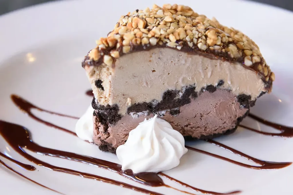 Layered chocolate peanut butter ice cream dessert with nuts and whipped cream.