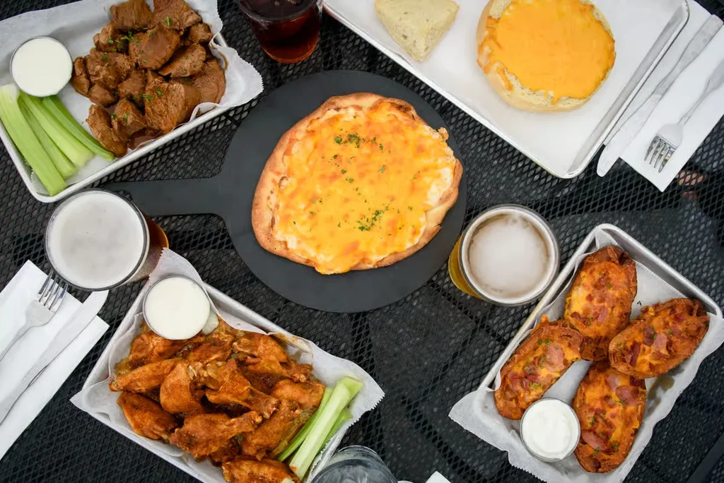 Overhead view of a table with various appetizers, pizza, and beer.