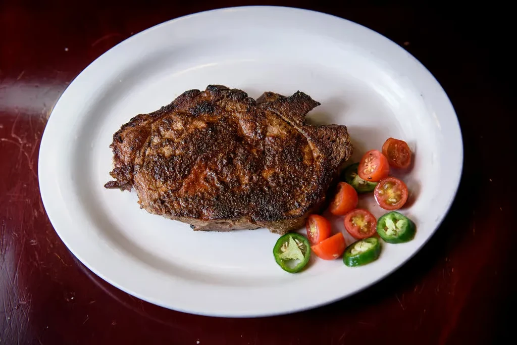 Well-seared steak, cherry tomatoes, and jalapeños on a white plate.