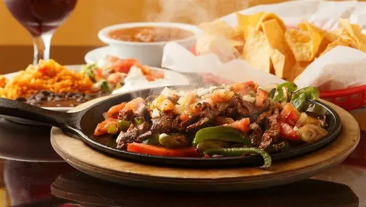 Sizzling fajita platter with meat, peppers, onions, rice, and chips.