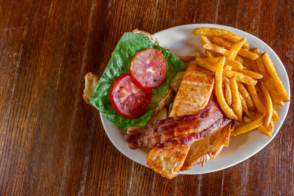 Grilled protein sandwich with bacon, lettuce, tomato, and french fries.