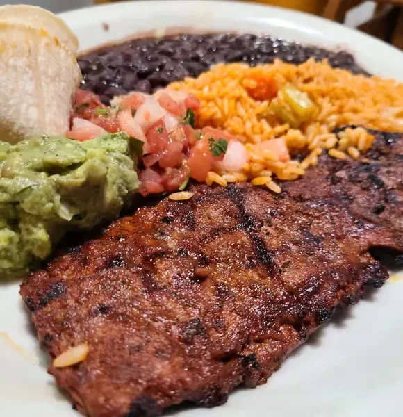 Grilled steak, Mexican rice, black beans, guacamole, salsa, and tortilla.
