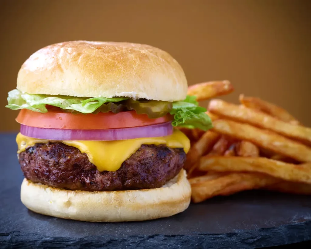 A close-up of a cheeseburger and french fries on a dark surface.