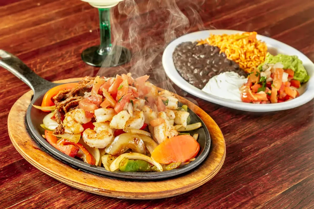 Hot fajitas with shrimp, beef, peppers, onions, rice, beans, guacamole.