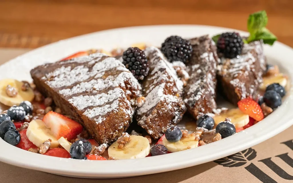 French toast with powdered sugar, berries, banana, nuts, and mint.