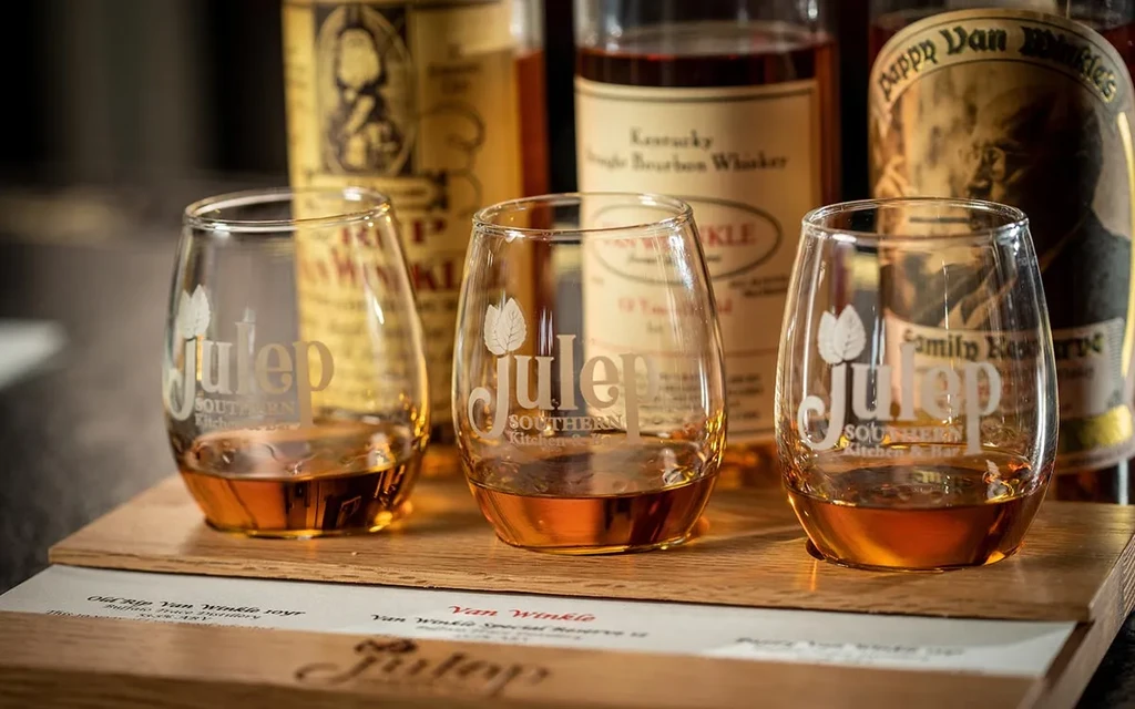 Three etched glasses of whiskey on a board, with tasting menu.