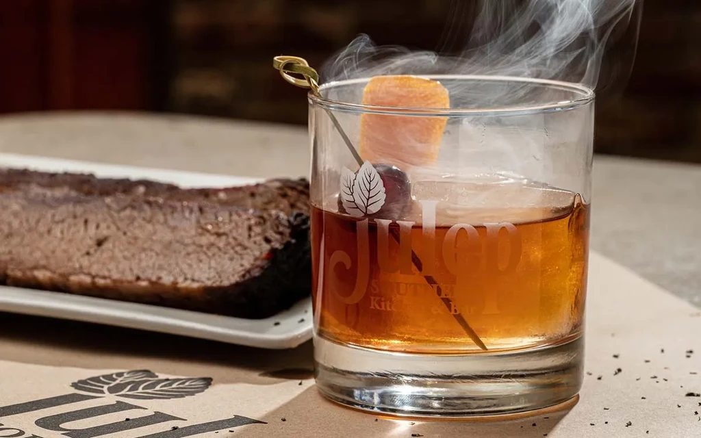 Smoky Julep cocktail with cherry, orange peel, and blurred brisket.