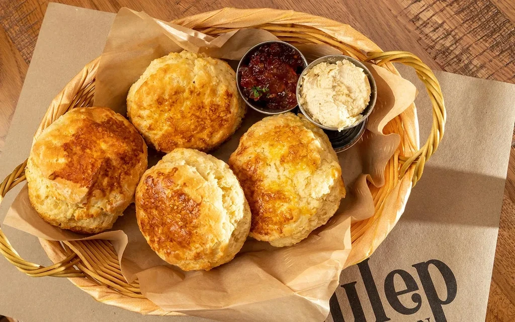 Wicker basket with homemade scones, jam, and cream on a placemat.