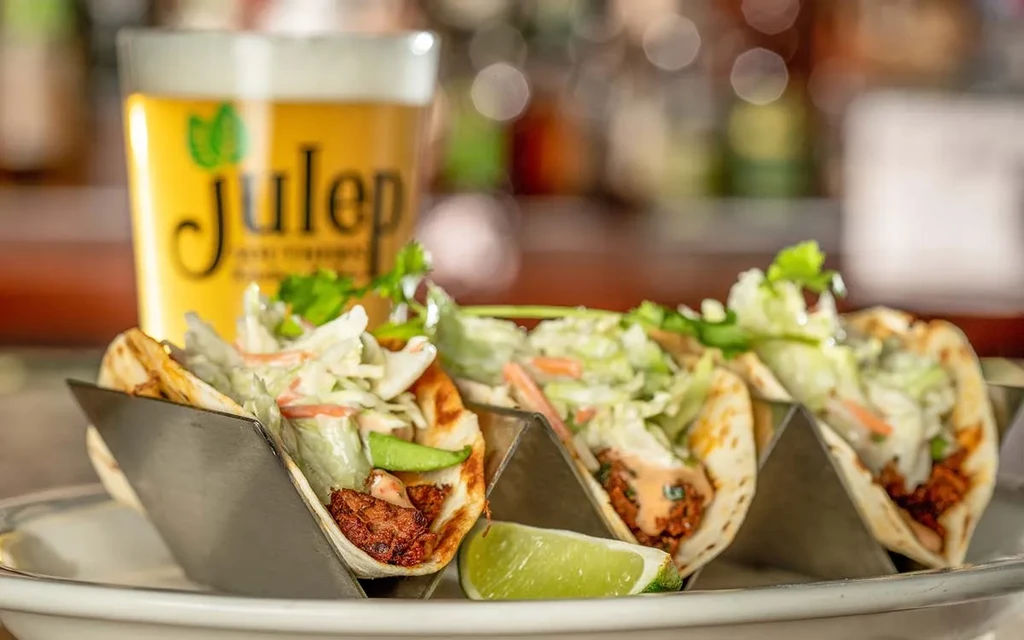 Three tacos with meat, cabbage, cilantro, lime, and Julep beer.