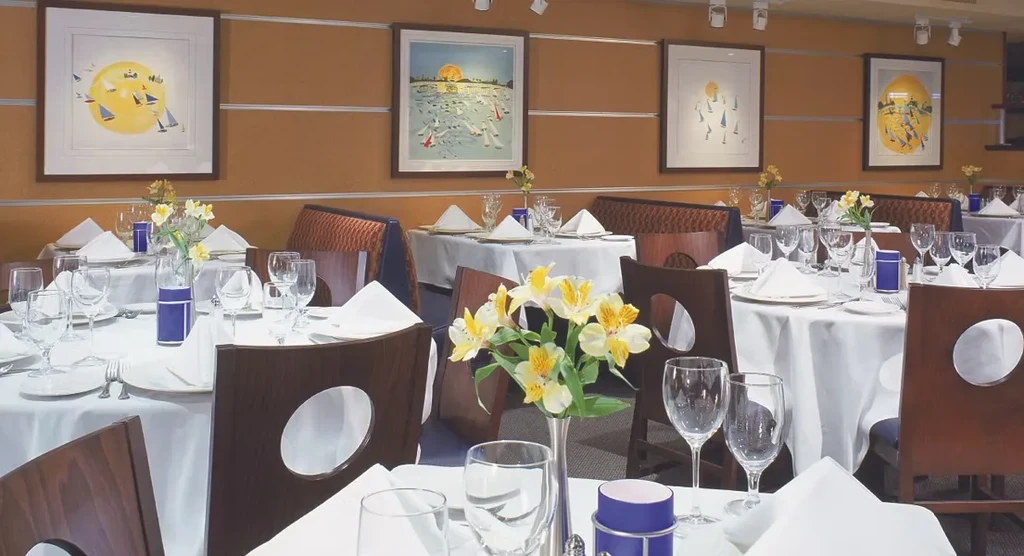 Empty restaurant dining room with white-clothed tables and boat art.