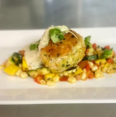 Golden patty with creamy sauce and herbs on colorful vegetables.