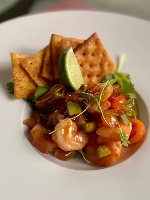 Shrimp ceviche with avocado, red vegetables, lime, and crackers.
