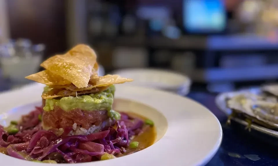 Cylindrical tuna tartare with guacamole, rice, chips, and pickled cabbage.